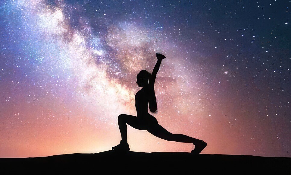 An image of a female silhouette doing yoga atop a mountain. Behind the figure is a galaxy swirl of stars and emission nebulae.